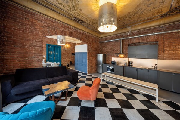 A modern kitchen with a checkered floor, a sofa, and a dining area with a blue door.