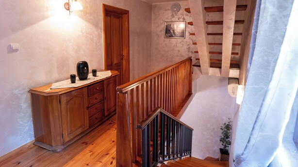 A wooden staircase with a railing, a wooden cabinet with drawers, a wall-mounted light fixture, and a framed picture on the wall.