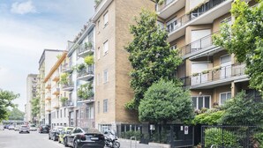 A row of multi-story residential buildings with balconies, parked cars, and a clear sky. - Easylife - Modern apartment in Bocconi (Milano)