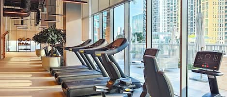 Un gimnasio con cintas de correr, equipo de ejercicio, ventanas amplias y una planta.