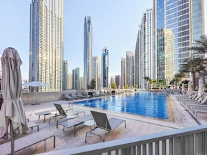 Ein Pool auf dem Dach mit Liegestühlen und Sonnenschirmen, umgeben von Hochhäusern.