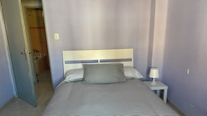 Una cama bien hecha con ropa de cama a rayas, una mesita de noche con una lámpara y una puerta que da a un baño.