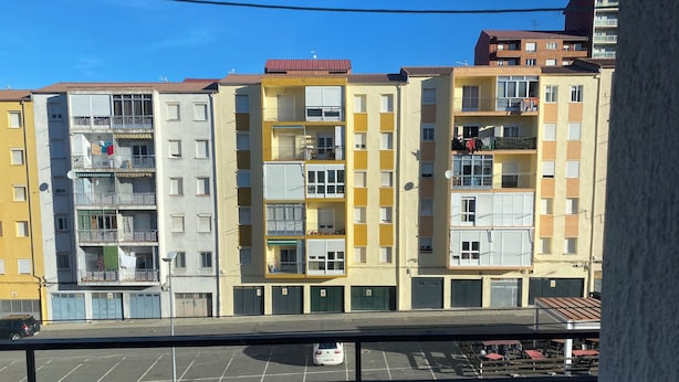 Una hilera de edificios residenciales de varios pisos con balcones, un estacionamiento y un cielo azul despejado.