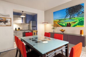 Een moderne keuken met roestvrijstalen apparatuur, een eethoek met een glazen tafel en rode stoelen, en een groot landschap op de muur.