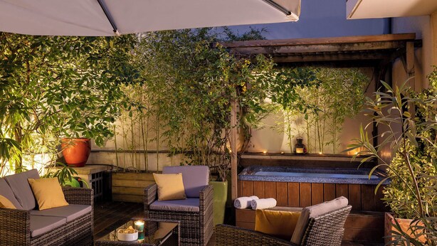 Une terrasse extérieure aménagée avec des meubles en osier, une petite table avec des bougies et un banc en bois.