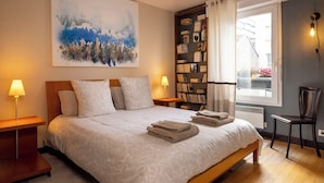 Une chambre à coucher avec un grand lit, deux lampes de chevet, une bibliothèque, une fenêtre avec des rideaux et un radiateur.