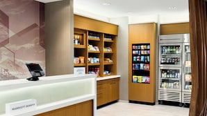 A hotel lobby with a self-service kiosk, wooden shelving stocked with snacks and beverages, and a refrigerated display case. - SpringHill Suites® by Marriott® Easton Bethlehem (Easton)