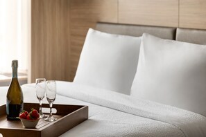 A neatly made bed with white linens, a tray with a bottle of wine, two glasses, and a bowl of strawberries. - SpringHill Suites® by Marriott® Easton Bethlehem (Easton)