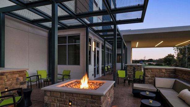 An outdoor patio with a stone fire feature, seating, and a glass-enclosed area. - SpringHill Suites® by Marriott® Easton Bethlehem (Easton)