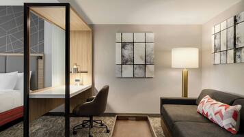 A modern hotel room with a bed, a desk, a chair, a sofa, and artwork on the walls.
