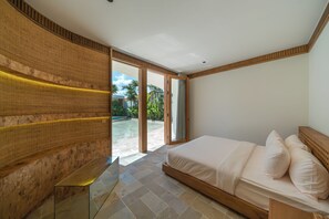 A bedroom with a bed, a glass table, a wooden wall, and a sliding glass door leading to an outdoor area. - Babylon (Cemagi)