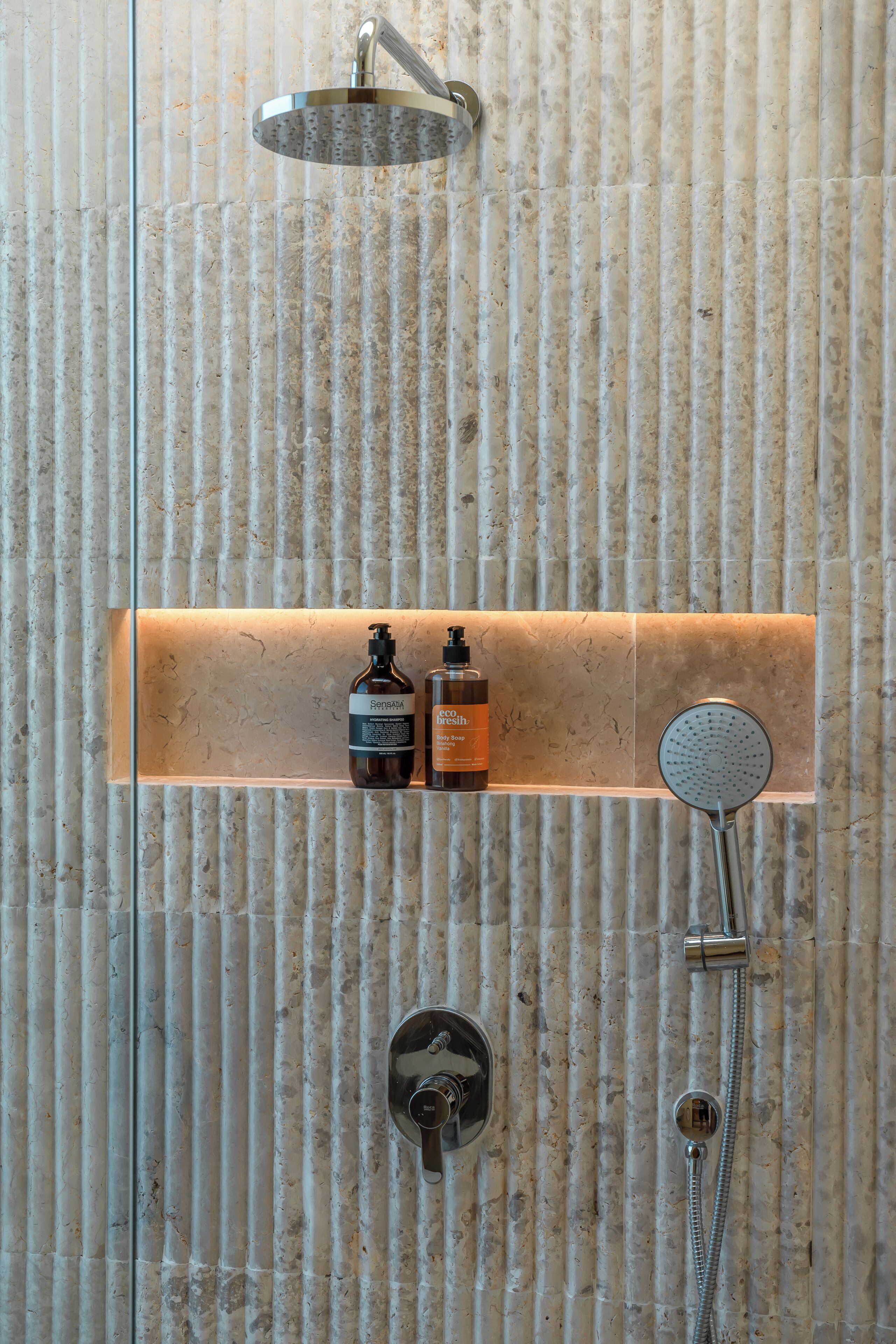 A bathroom with a shower, a soap dispenser, and a bottle of shampoo.