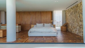 A modern bedroom with a large bed, wooden panel walls, and a stone accent wall. - Babylon (Cemagi)