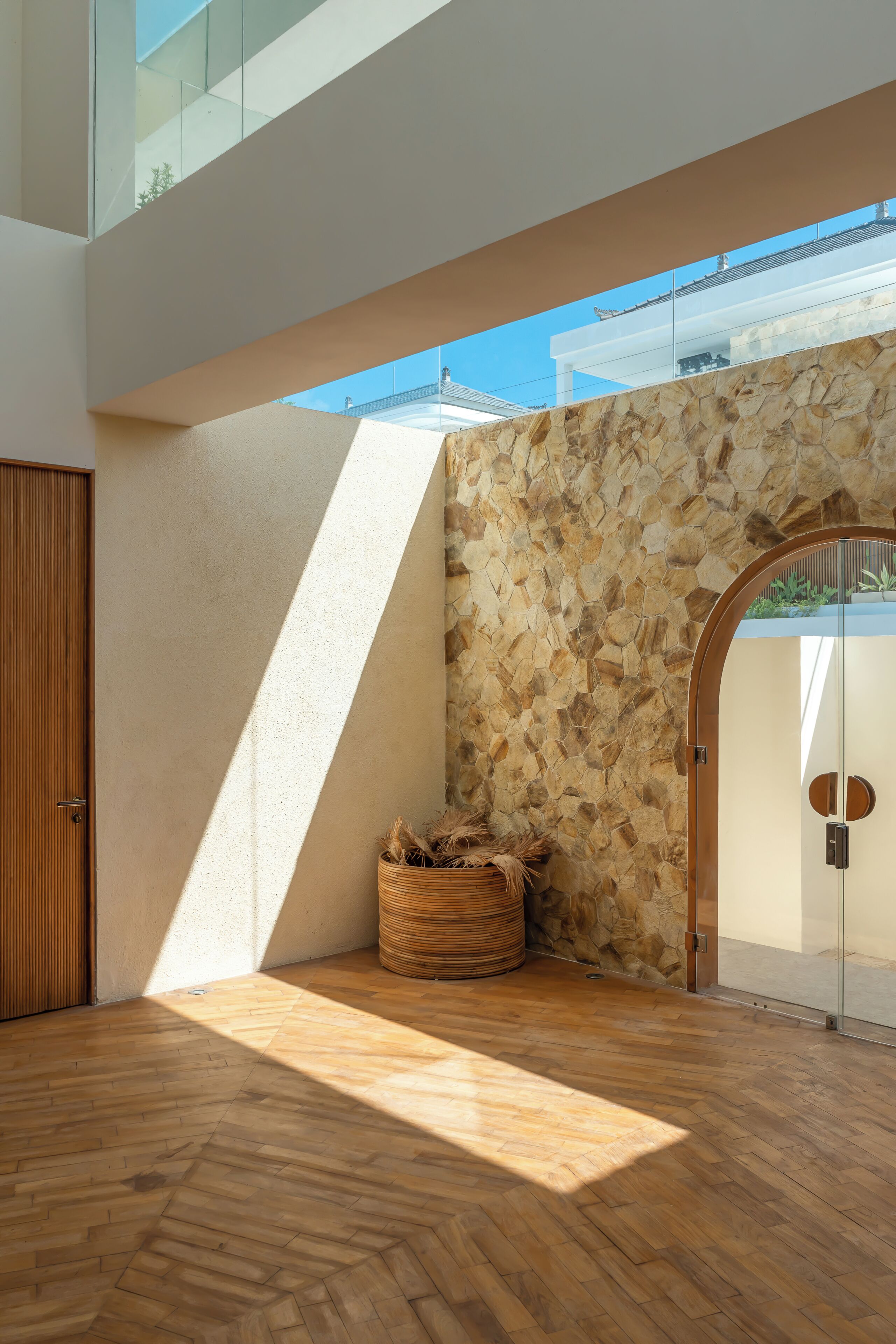 Een modern interieur met een houten vloer in visgraatmotief, een stenen muur en een glazen deur naar buiten.