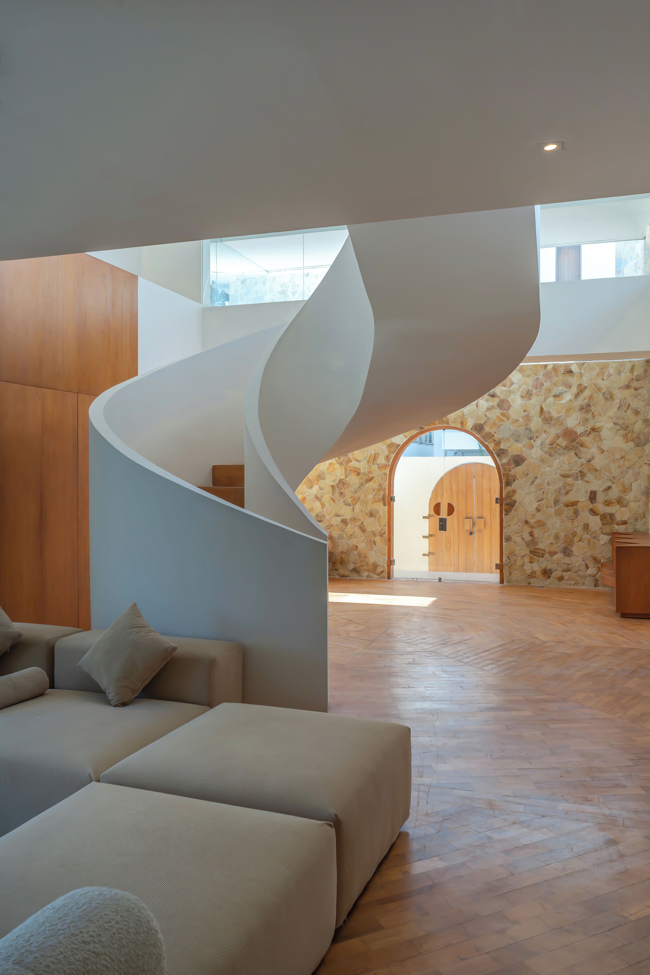 A modern interior with a spiral staircase, a stone wall, and a wooden door.