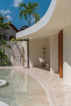 A modern outdoor pool area with a curved white wall, a palm tree, and a potted plant. - Babylon (Cemagi)