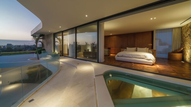A modern bedroom with a large bed, a glass-enclosed balcony, and a view of the city. - Babylon (Cemagi)