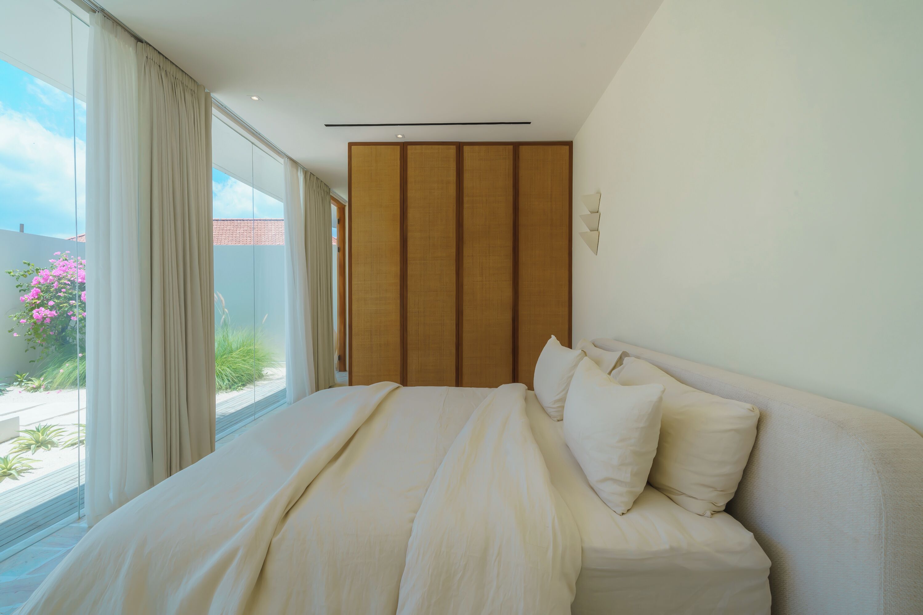 A bedroom with a large bed, a sliding wooden door, and a view of the outdoors.