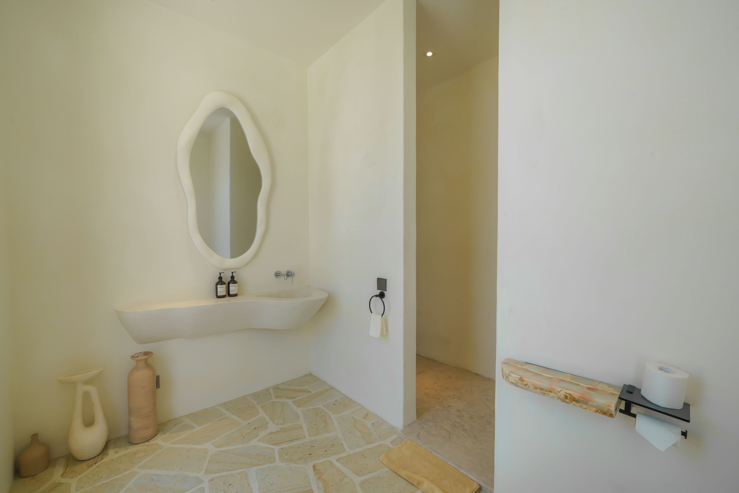 A bathroom with a stone floor, a white sink, a mirror, and a towel rack.