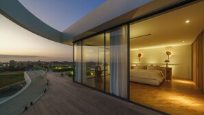A modern bedroom with a glass wall, a curved balcony, and a view of the cityscape. - Babylon (Cemagi)