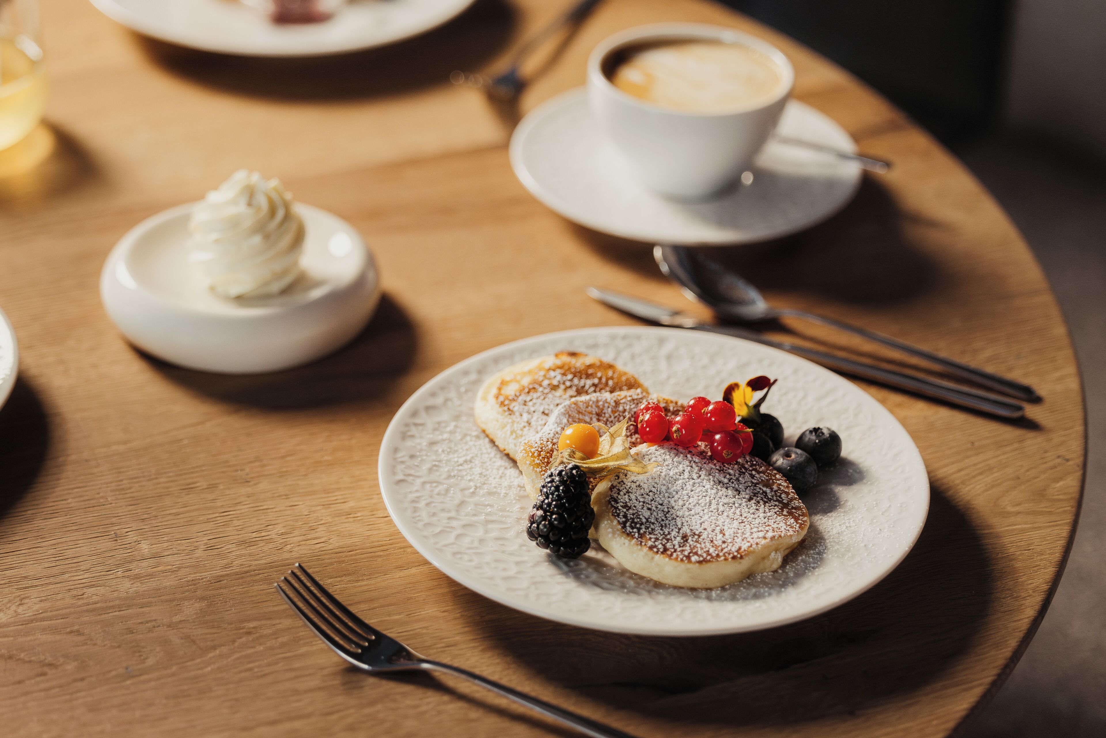 A dessert plate with pancakes, berries, and powdered sugar on a wooden table.