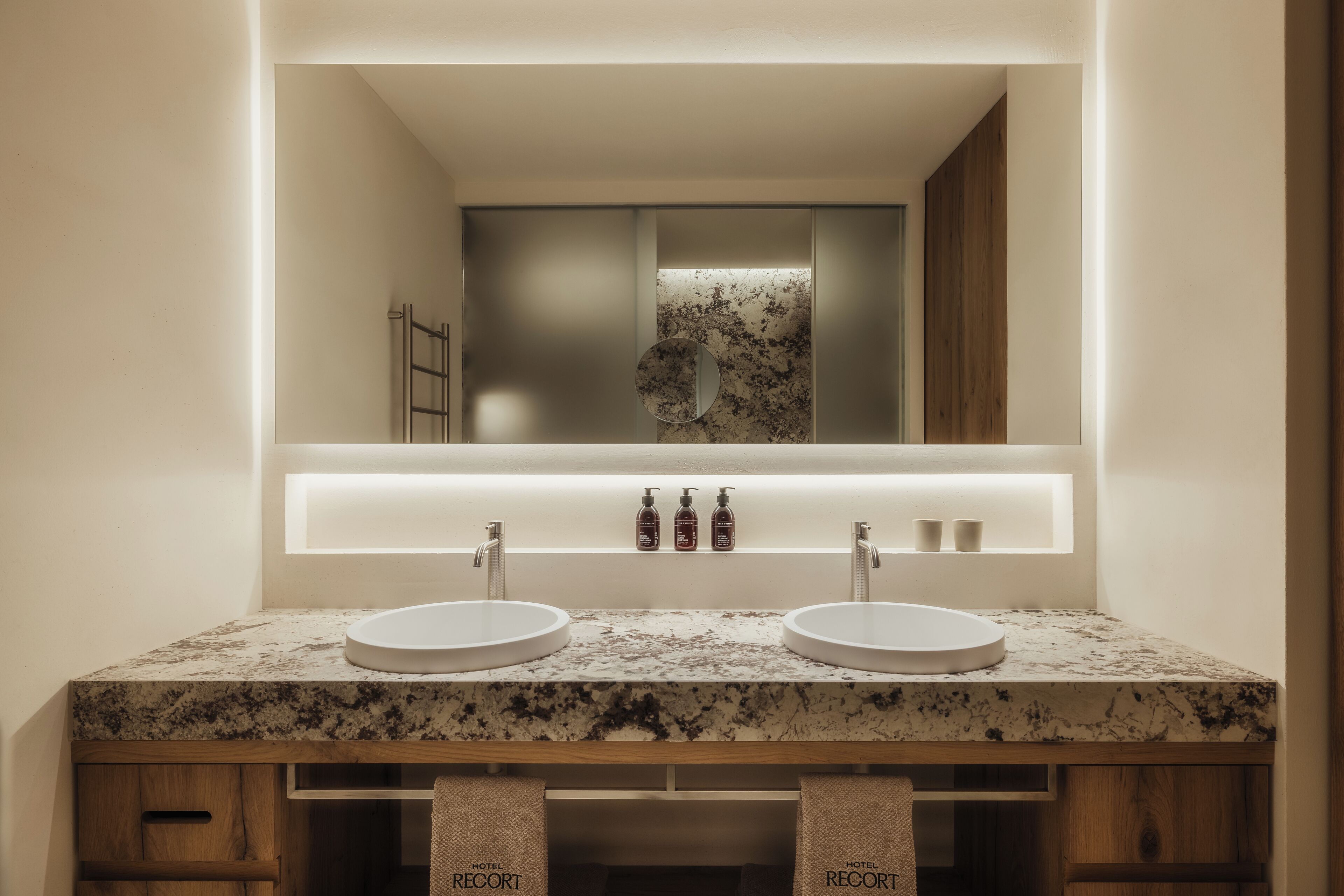 Un baño moderno con dos lavamanos, un espejo grande y un mueble tocador con encimera de mármol.