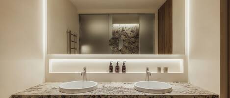 Un baño moderno con dos lavamanos, un espejo grande y un mueble tocador con encimera de mármol.