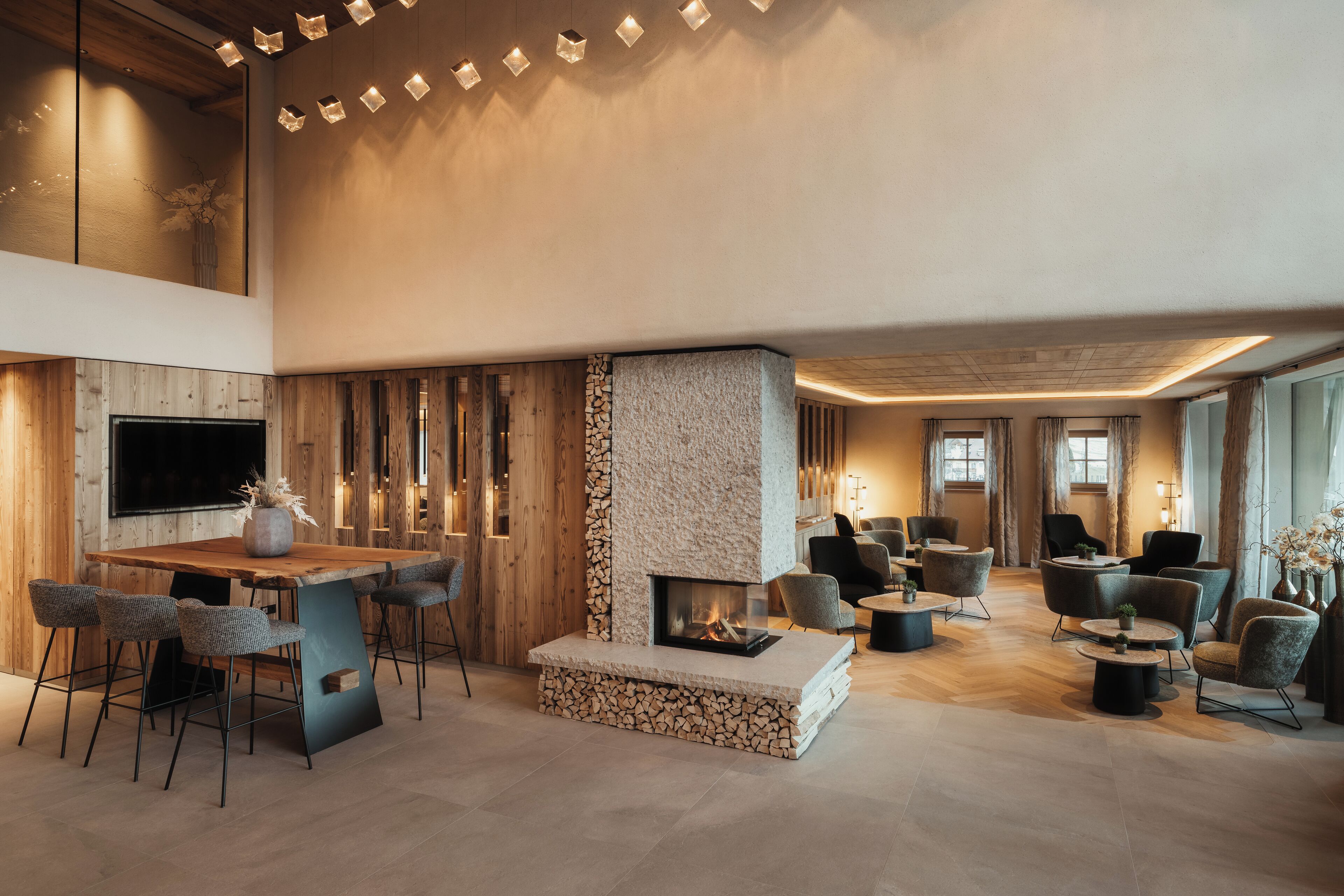 A spacious lounge area with a central seating arrangement, a fireplace, and a television mounted on the wall.