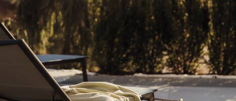 A sunlit outdoor seating area with a lounge chair and a woven basket.
