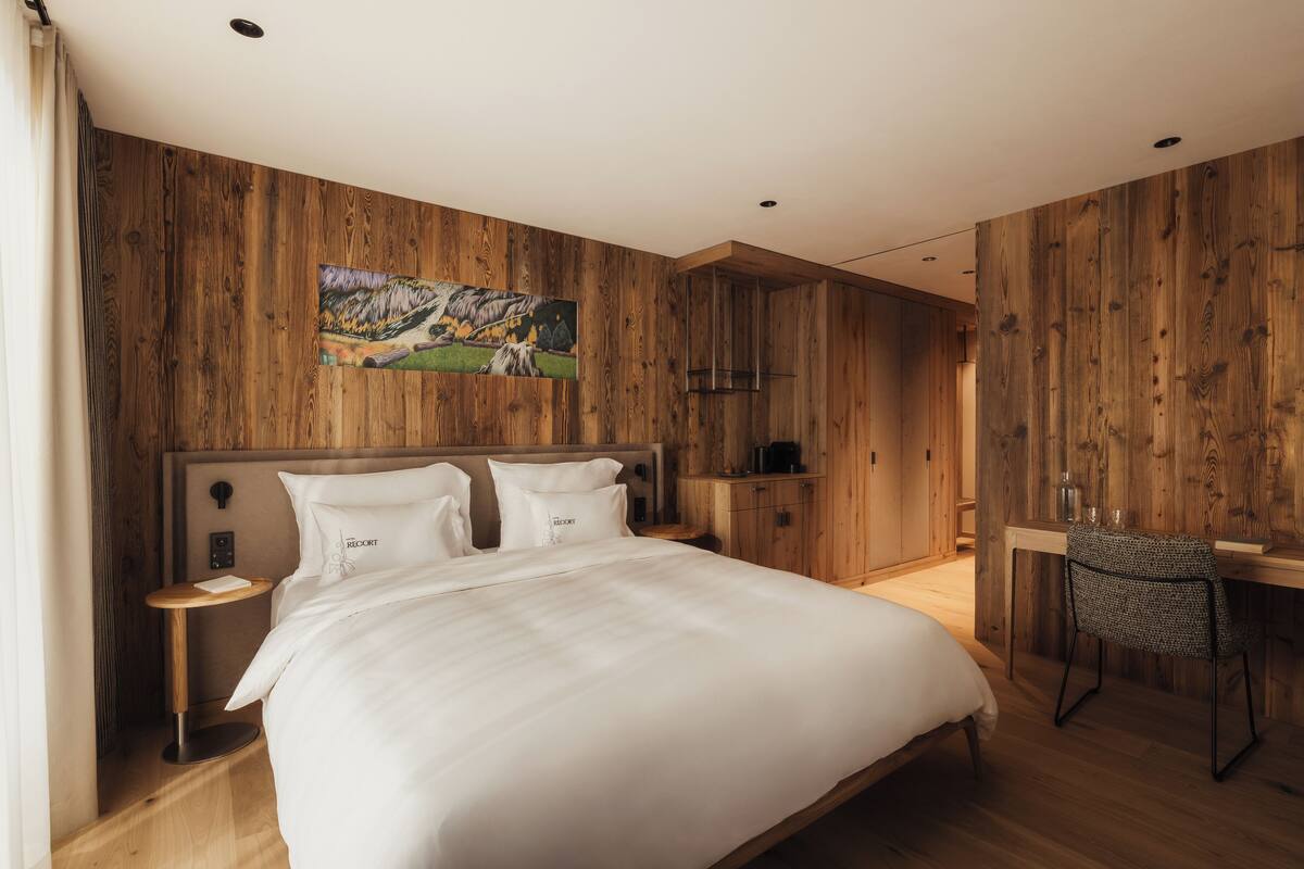 Ein Schlafzimmer mit einem großen Bett, Holzwänden, einem Gemälde, einem Schreibtisch und einem Stuhl.
