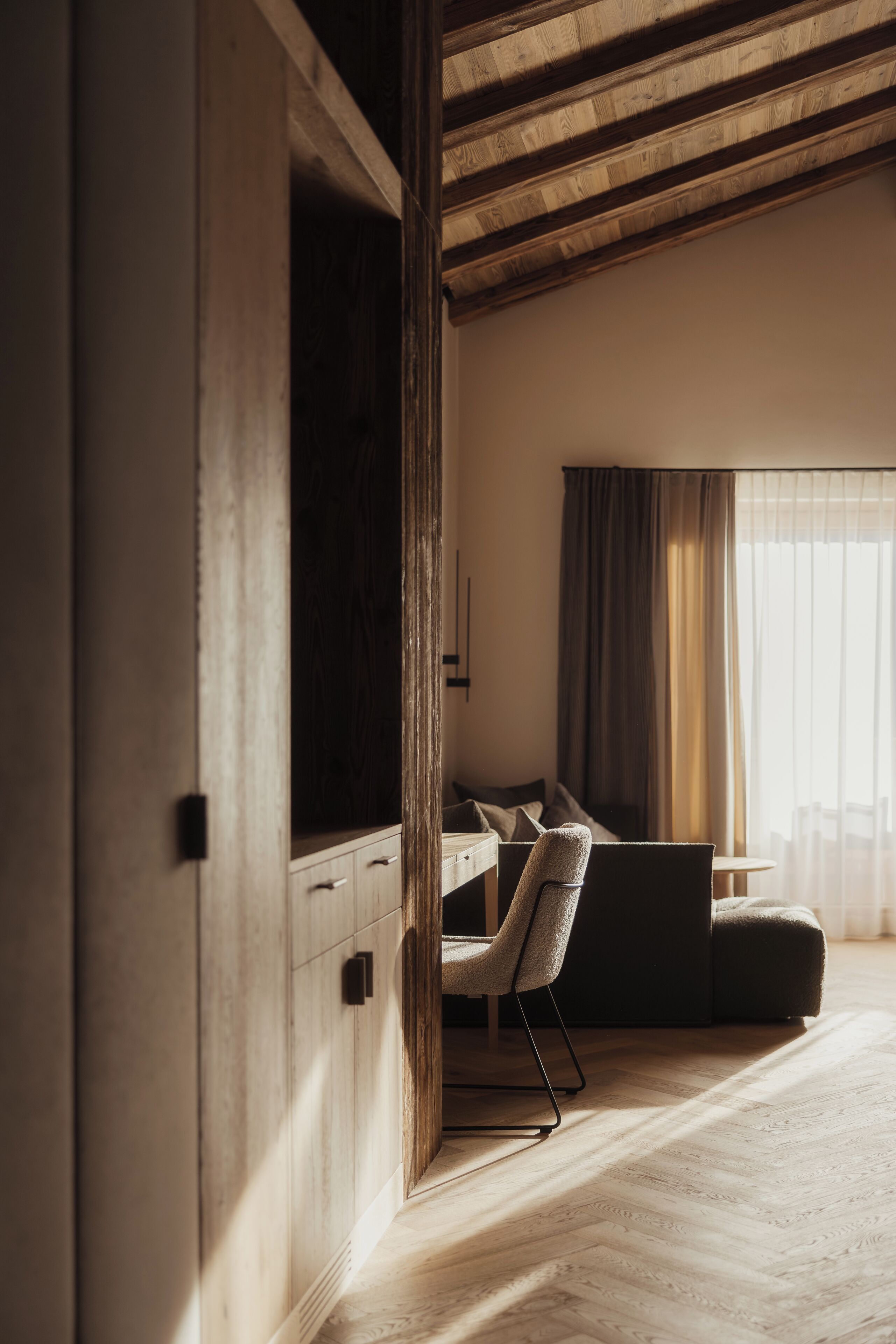 A modern room with a wooden ceiling, a large window with curtains, a sofa, and a desk with a chair.