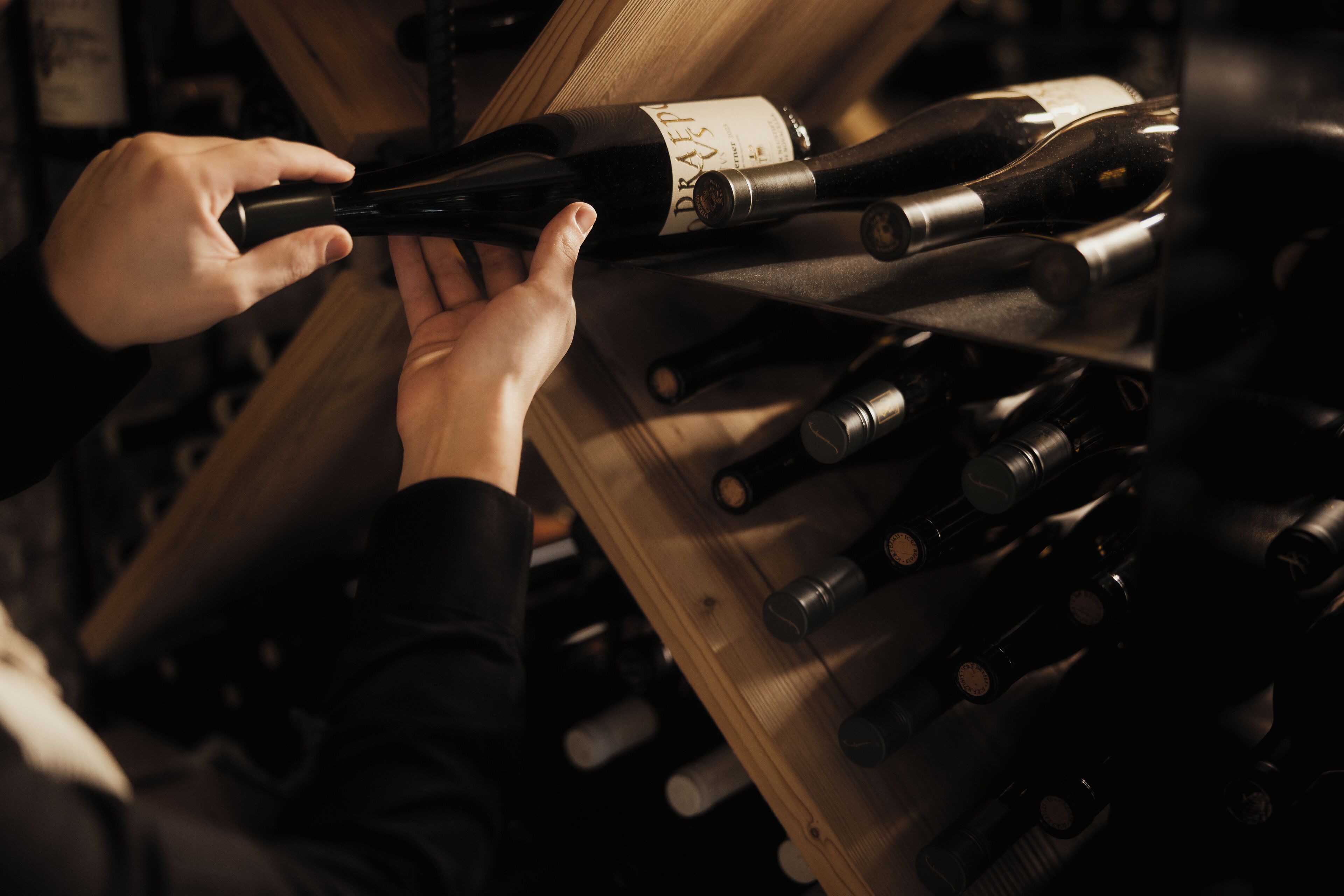 A person selecting a wine bottle from a wooden rack filled with various bottles.