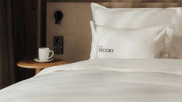 A hotel room with a wooden headboard, a painting of a rabbit, a white pillow with "RECORD" text, a bedside table with a white cup, and a power outlet.