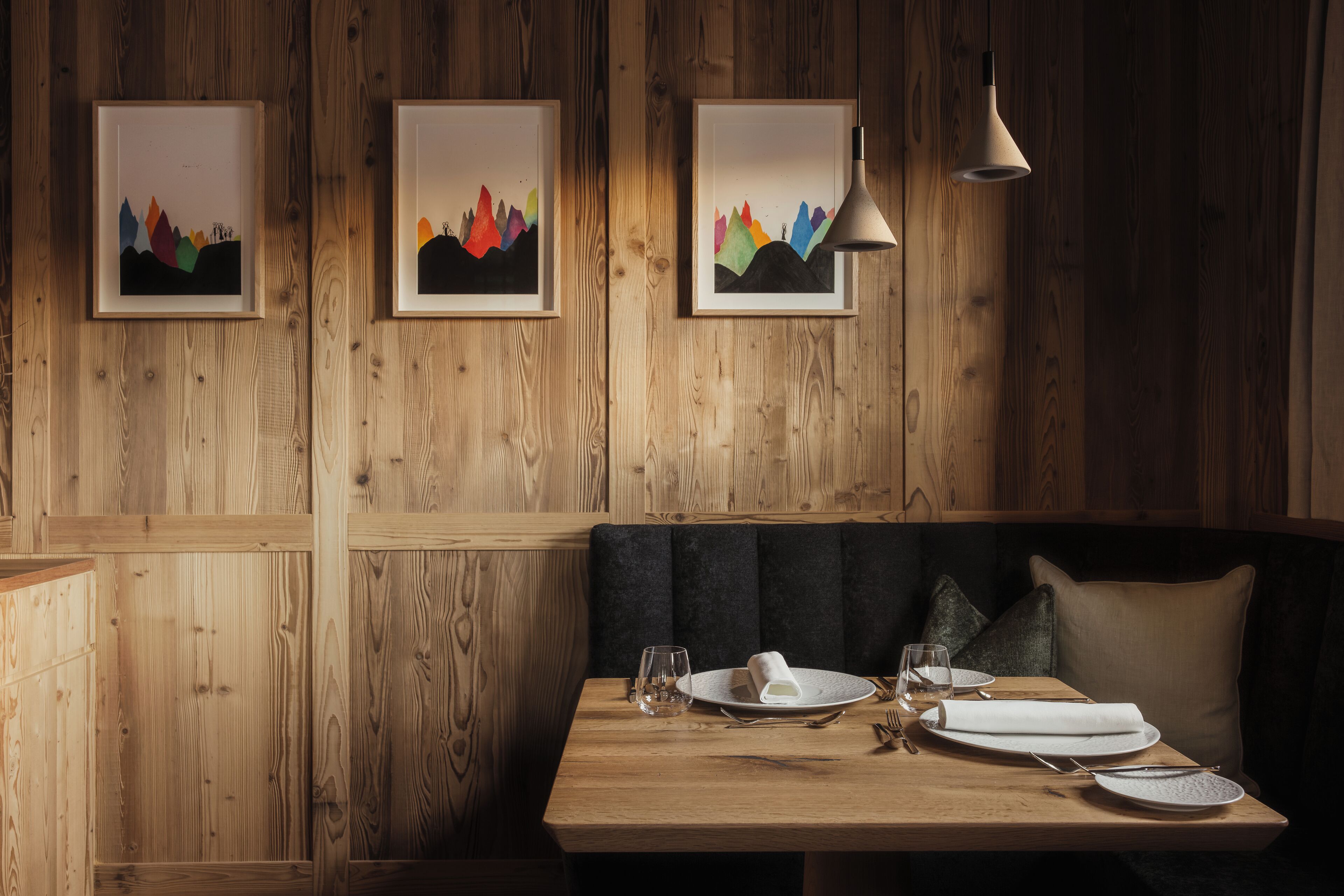 A wooden wall with framed artwork, a wooden table set for dining, and a bench with cushions.