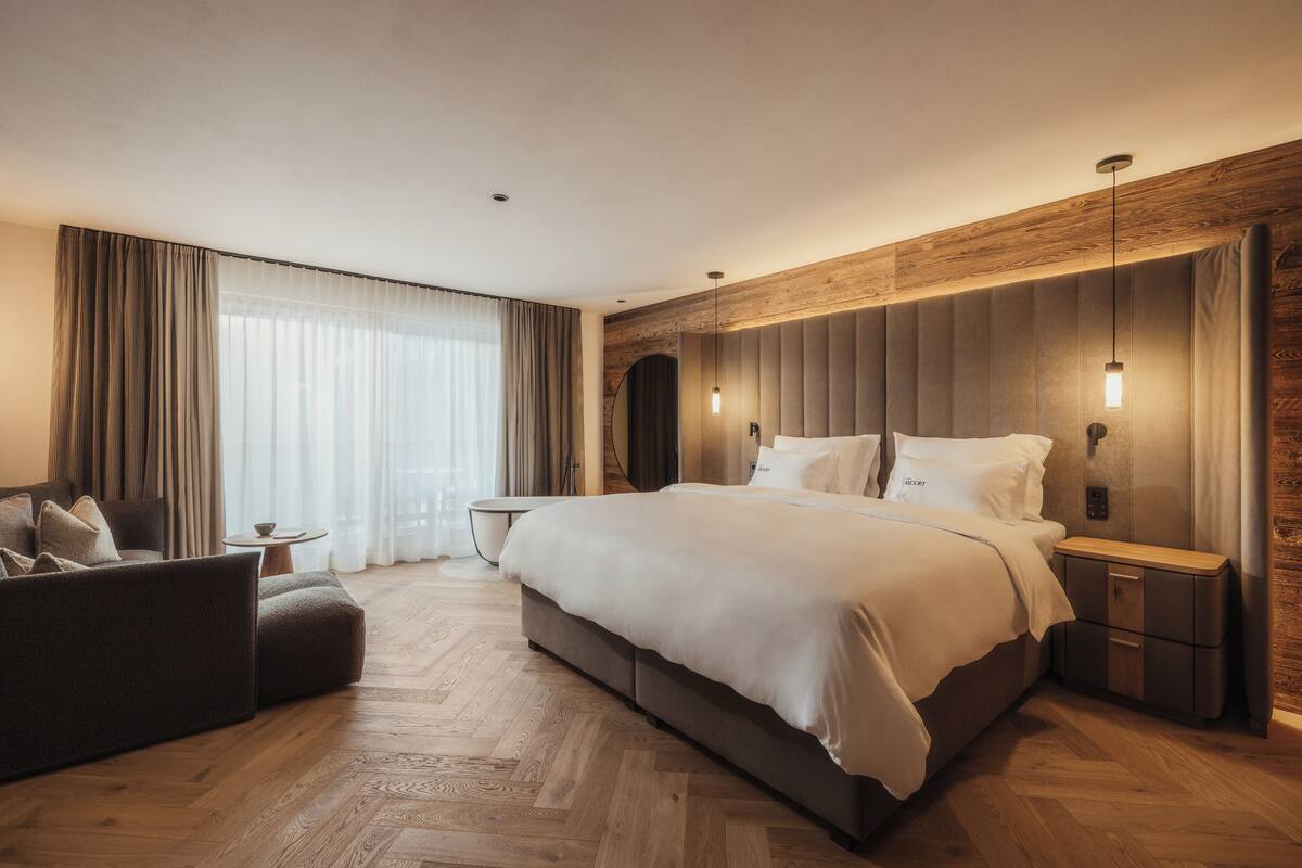 Ein modernes Hotelzimmer mit einem großen Bett, einer Couch, einem kleinen Tisch und einem Nachttisch.