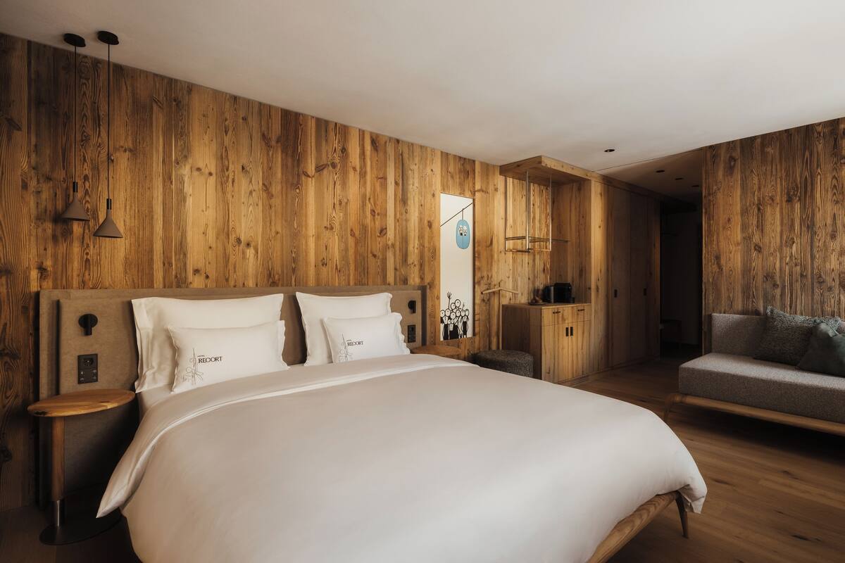 Ein Schlafzimmer mit Holzwand, einem Bett mit weißer Bettwäsche, einem Nachttisch, einer Lampe und einem Sofa.