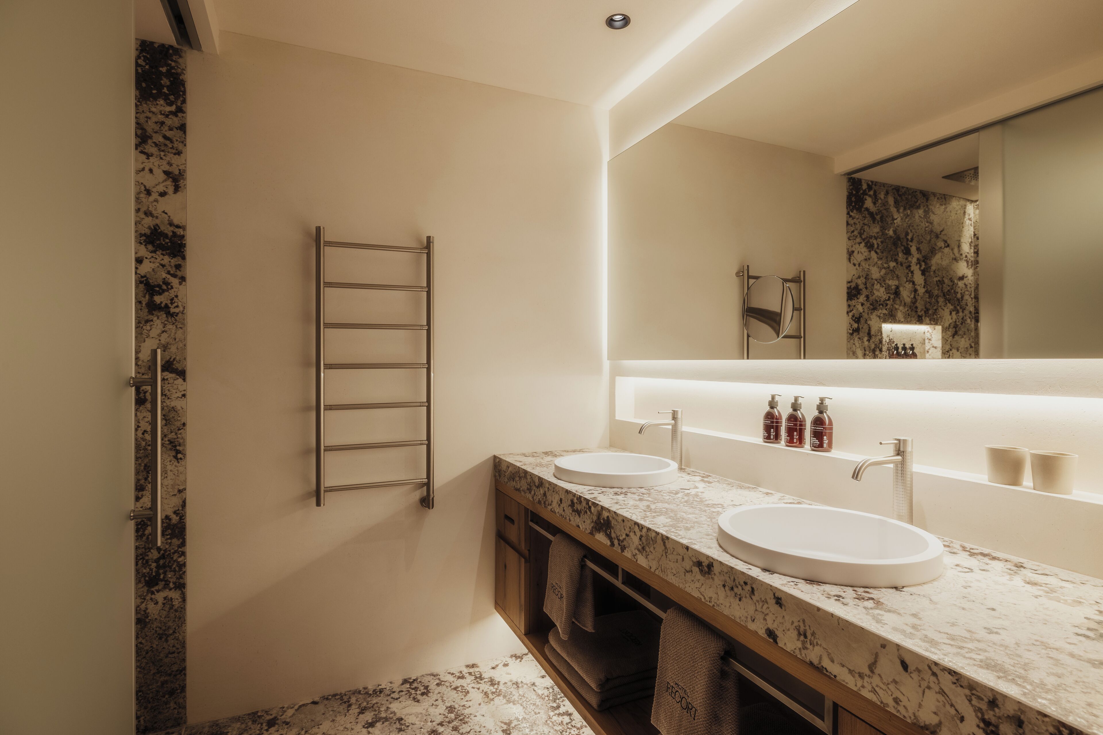 A modern bathroom with two sinks, a large mirror, and a towel rack.