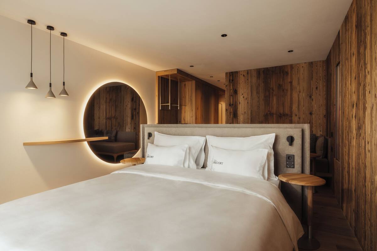 Ein modernes Schlafzimmer mit einem großen Bett, einem runden Spiegel, Pendelleuchten und einer Holzwandverkleidung.