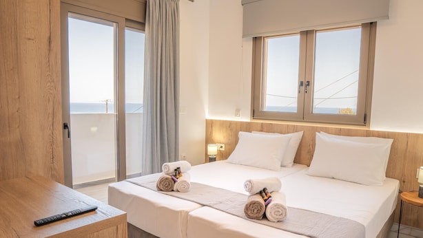 A hotel room with a bed, two bedside tables, a desk, and a view of the sea. - Villa Leandros With Pool & bbq (Agios Nikolaos)
