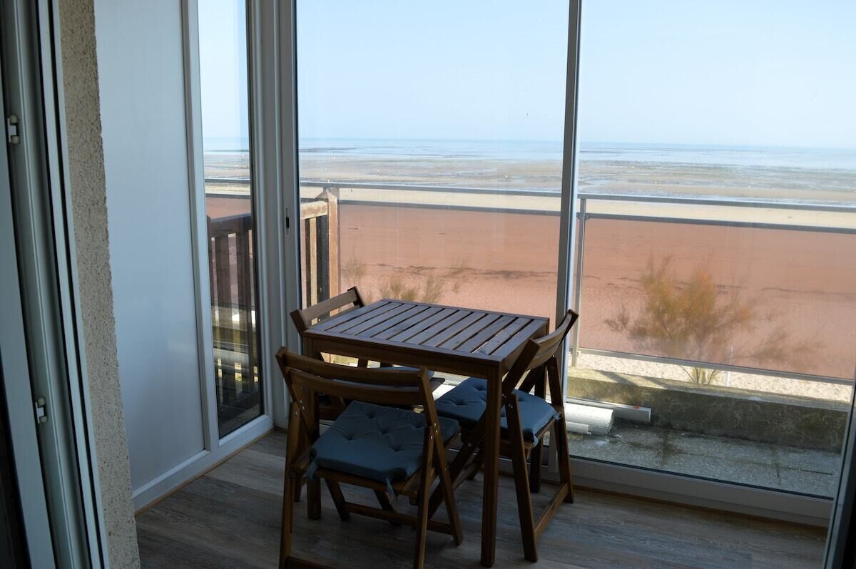 Un balcon avec une table et des chaises en bois, offrant une vue sur la plage.