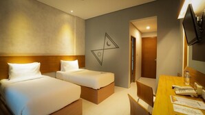 A hotel room with two beds, a desk with a chair, a television, and a wall with a geometric design. - NITE & DAY MDC Gadog (Megamendung)