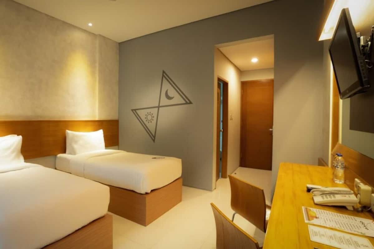 A hotel room with two beds, a desk with a chair, a television, and a wall with a geometric design.