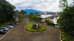 A residential street with parked cars, a central roundabout, and houses with sloped roofs. - NITE & DAY MDC Gadog (Megamendung)