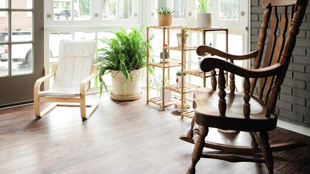 A room with a wooden rocking chair, a white chair, and a plant shelf by a large window. - We can all stay together, everyone has room, the dog can come, and getting where we need to go is easy. (Montgomery)