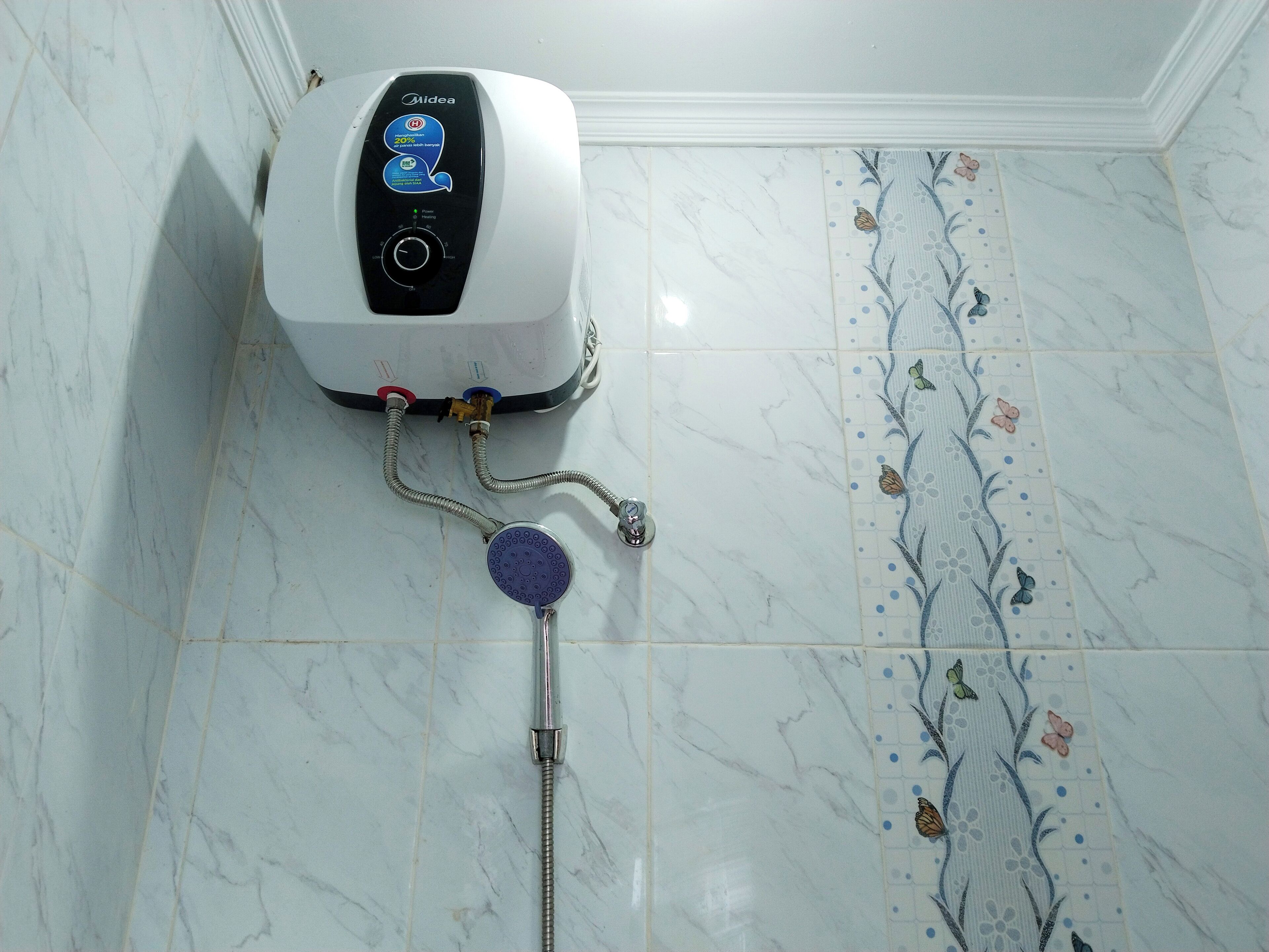 Une salle de bain avec un chauffe-eau blanc de la marque Midea, une douche avec un carrelage au motif floral et un mur recouvert de carreaux de marbre.