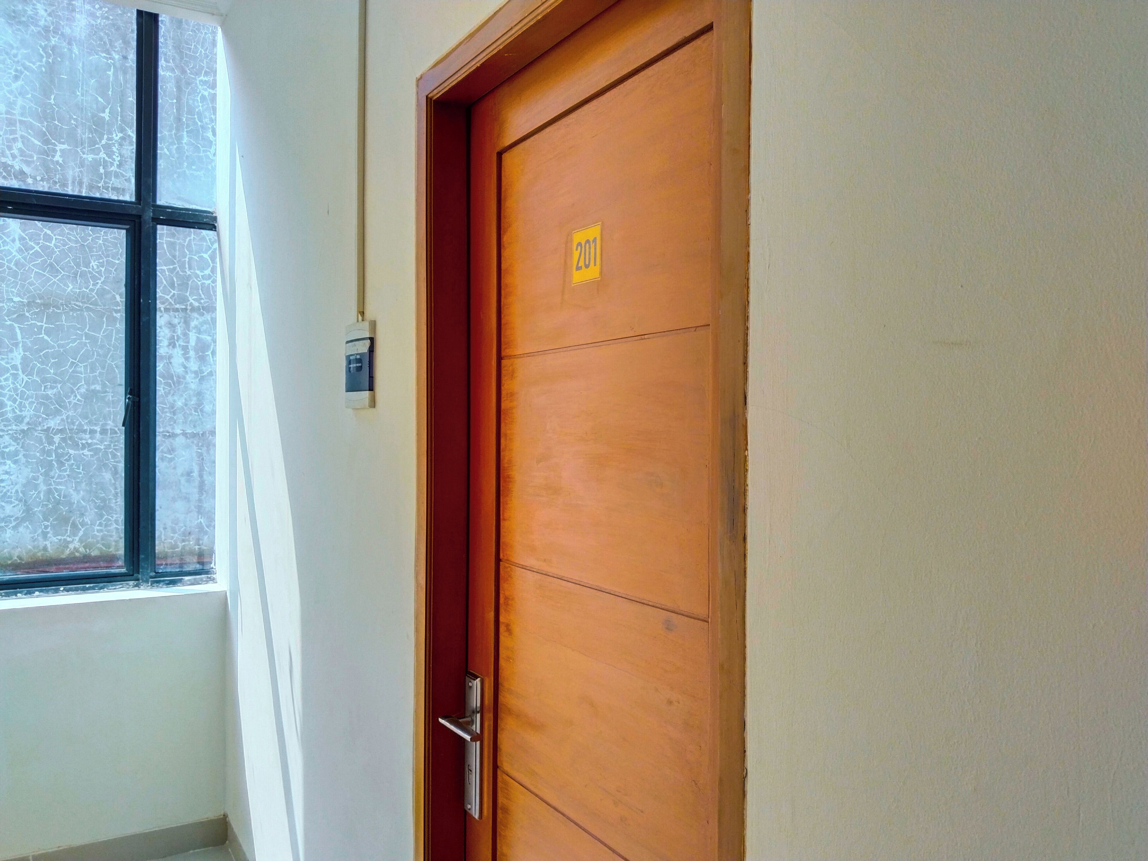 A wooden door with a number plate, a window with a cross pattern, and a wall-mounted electrical outlet.