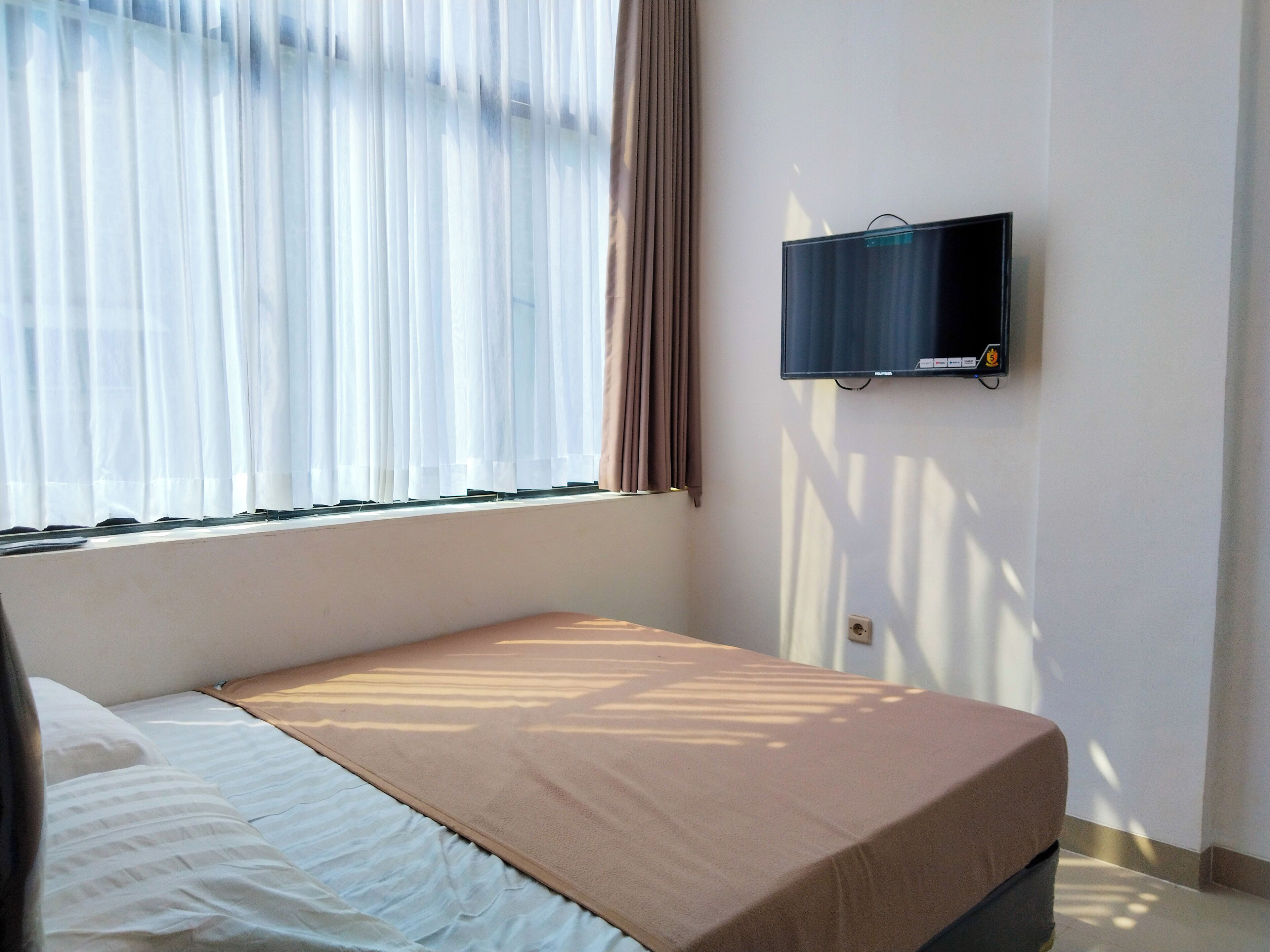 A room with a bed, a TV mounted on the wall, and a window with curtains.