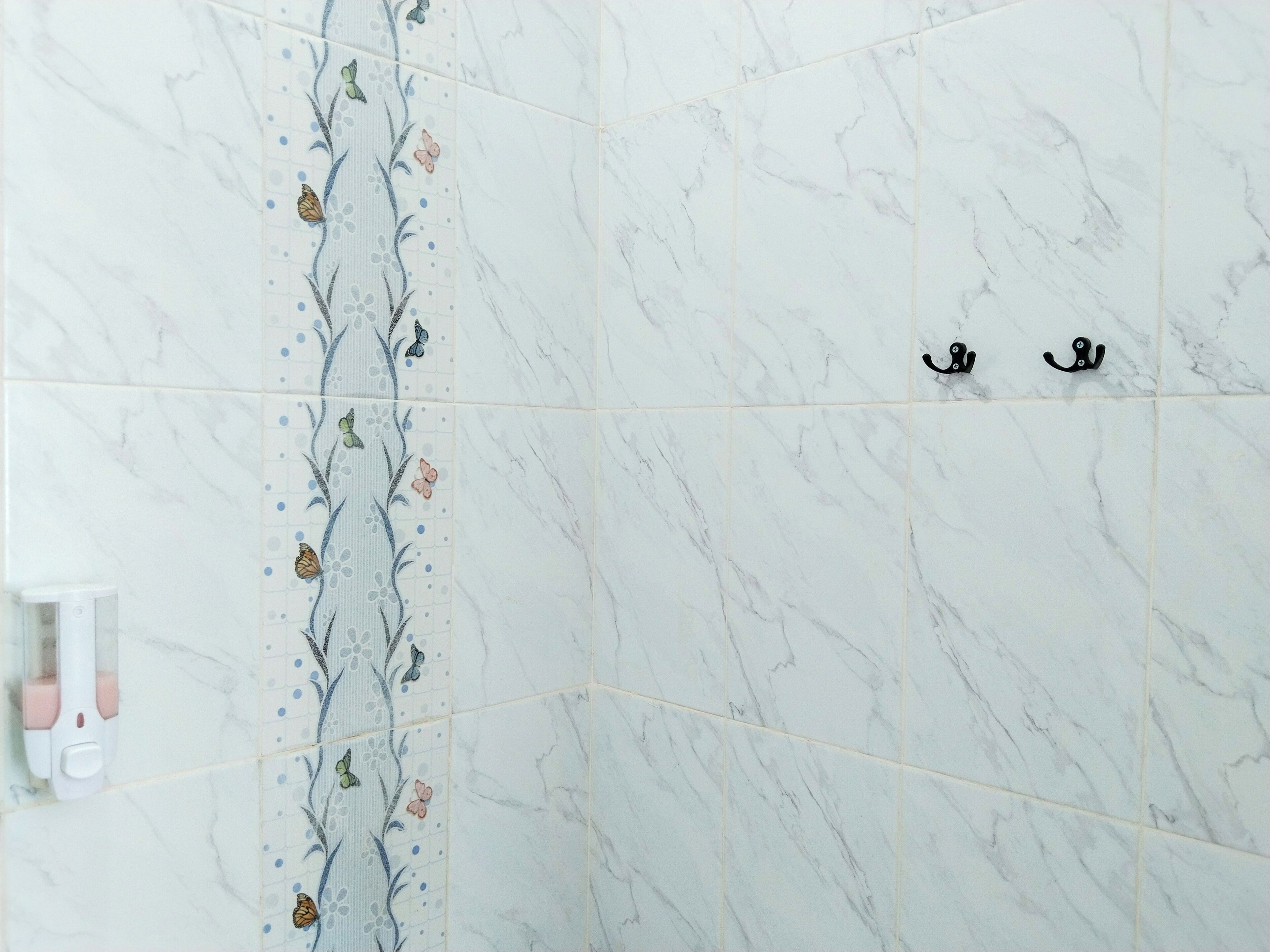 A bathroom with white marble tiles, a floral pattern on one wall, and a black towel rack.