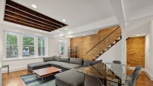 Ein modernes Wohnzimmer mit einem Ecksofa, einem Glastisch und einer Treppe an einer Ziegelwand.