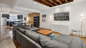 Ein modernes Wohnzimmer mit Ecksofa, Holztisch und Essbereich, im Hintergrund eine Küche.